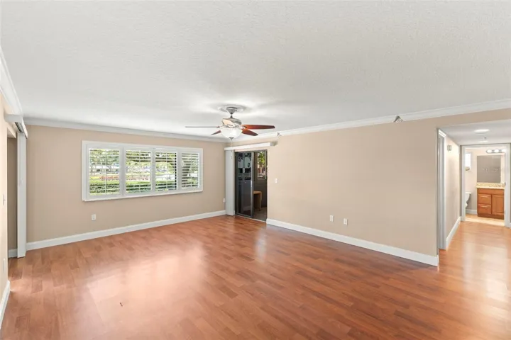 Wood-look flooring, crown molding, plantation shutters, and a ceiling fan enhance the comfort and appeal of the spacious living room.