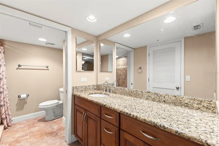 The ensuite bath features a granite-topped vanity, wood cabinetry, recessed lighting, and generous counter space.