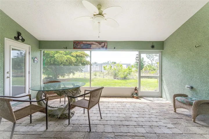 The covered and enclosed rear porch features a ceiling fan and paver flooring.