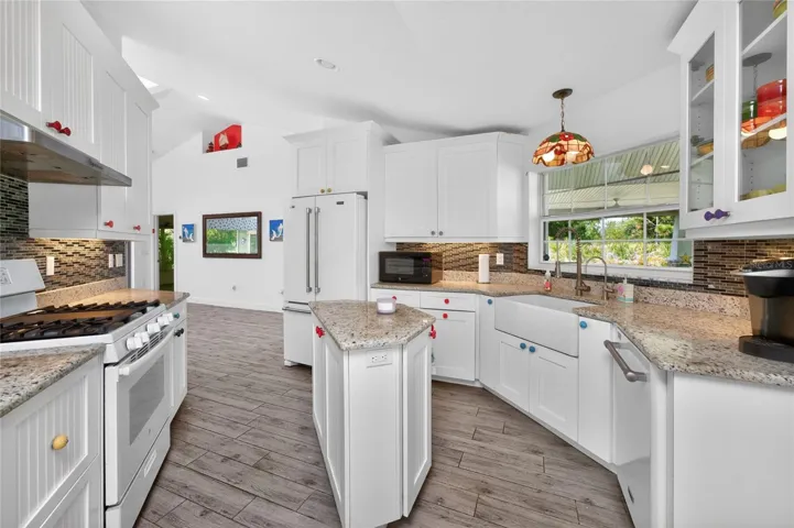 The kitchen has plank tiled flooring, a GE gas stove and cottage style cabinetry.