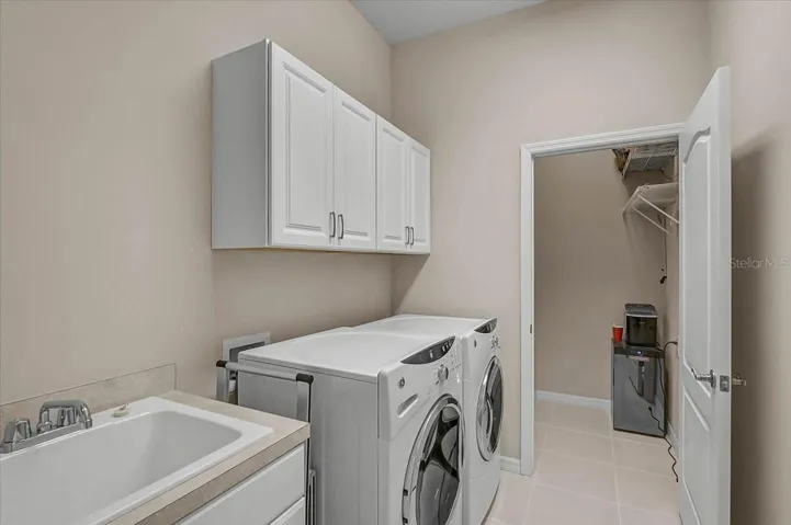 The spacious laundry room is equipped with a utility sink, built-in cabinetry, and access to an additional storage area that houses the air handler, providing convenient space for household essentials and seasonal items.