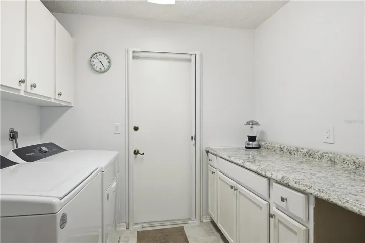 Convenient indoor laundry room complete with washer and dryer, upper storage cabinets, and a spacious folding counter with extra lover cabinetry.