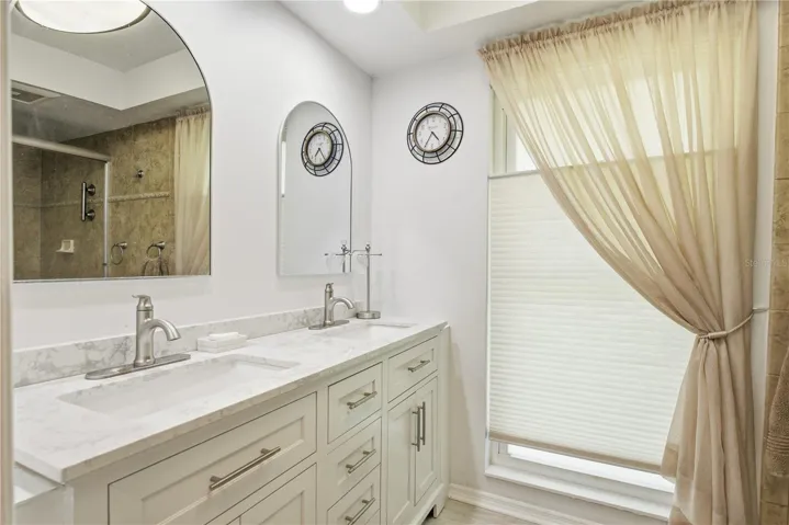 Primary bathroom featuring a long double vanity with stone countertops, ample cabinet storage, modern hardware, and matching arched mirrors.