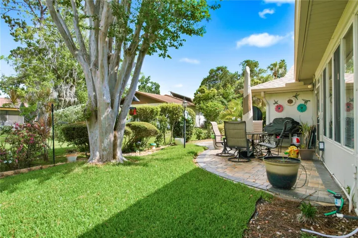 Beautiful landscaped backyard featuring a curved paver patio perfect for outdoor dining, a lush green lawn, and mature shade trees.