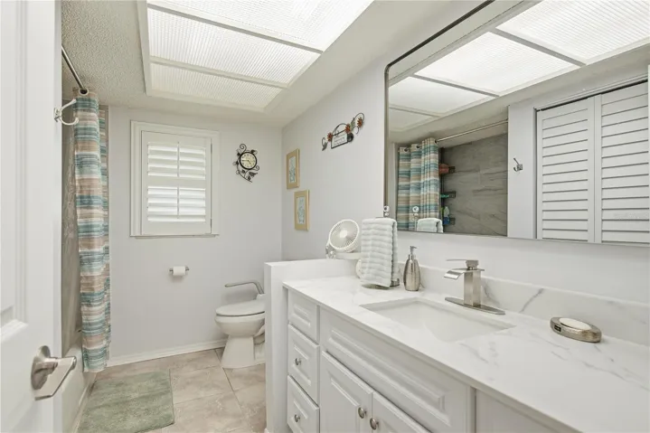 Updated secondary bathroom featuring a bright vanity with stone countertops, a large mirror, a tiled shower/tub combo, and a stylish plantation shudder window.