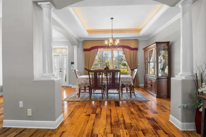 Dining room by entryway, tray ceiling, large windows, decorative columns, wood flooring, open floor plan leading to living room