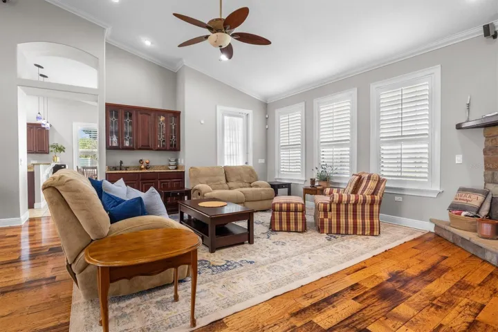 living room, gas fireplace, wood flooring, built in wet bar with sink, door leaving to patio, plantation shutters, high ceilings