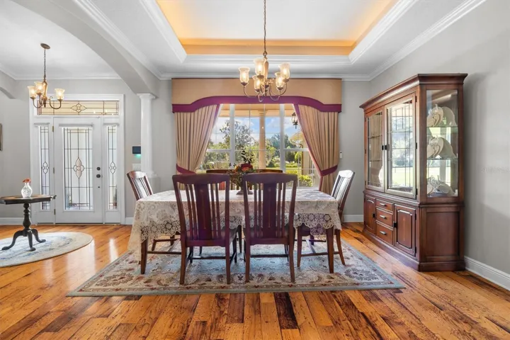 Dining room by entryway, tray ceiling, large windows, decorative columns, wood flooring, open floor plan leading to living room