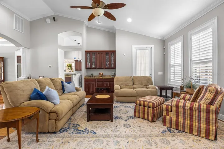 living room, gas fireplace, wood flooring, built in wet bar with sink, door leaving to patio, plantation shutters, high ceilings