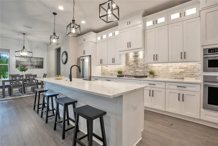 Designer chef's kitchen featuring quartz countertops, oversized center island, custom cabinetry, stainless steel appliances, and abundant natural light.