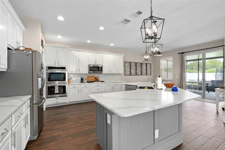kitchen with quartz countertops, wainescoting, custom backsplash, stainless steel farmers sink, pendant lights, built in ovens and a gas cooktop.