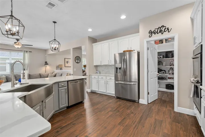 kitchen with quartz countertops, wainescoting, custom backsplash, stainless steel farmers sink, pendant lights, built in ovens and a gas cooktop.