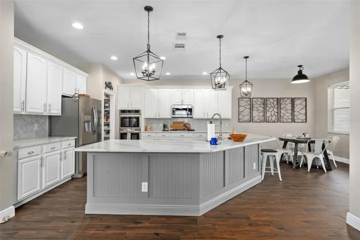kitchen with quartz countertops, wainescoting, custom backsplash, stainless steel farmers sink, pendant lights, built in ovens and a gas cooktop.
