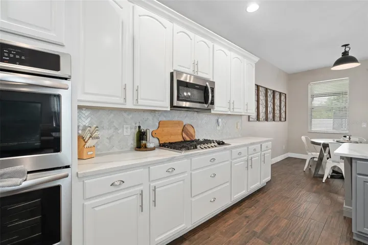 kitchen with quartz countertops, wainescoting, custom backsplash, stainless steel farmers sink, pendant lights, built in ovens and a gas cooktop.