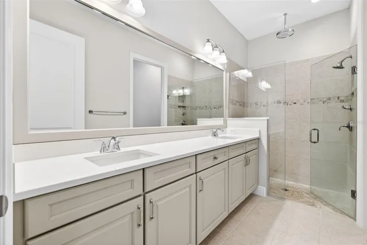 Double sink vanity in primary suite with glass enclosed shower