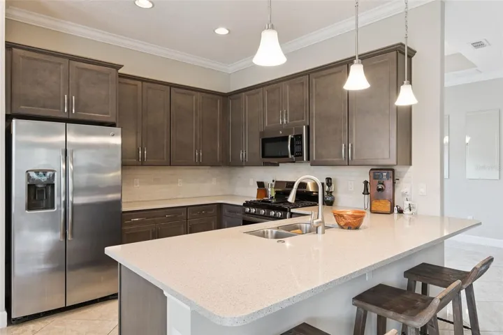 Kitchen breakfast bar w/ pendant lighting above & tumble stone backsplash underneath Kitchen cabinets