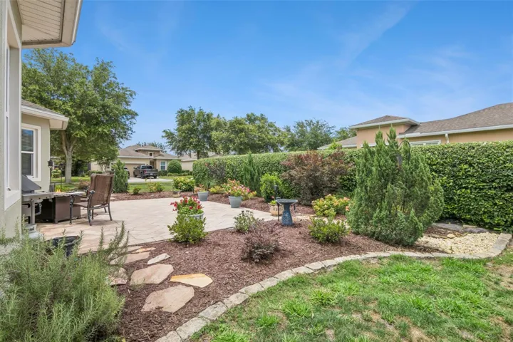 View of stone paver lanai & lush landscaping on a corner homesite