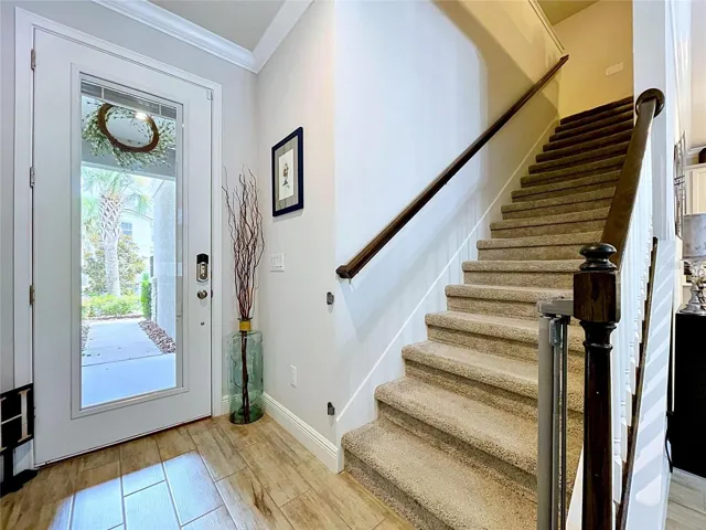 Step inside and immediately feel at home. This welcoming entry features wood-look tile flooring, crown molding, abundant natural light, and a dramatic staircase with dark wood accents that creates a warm and elegant first impression.