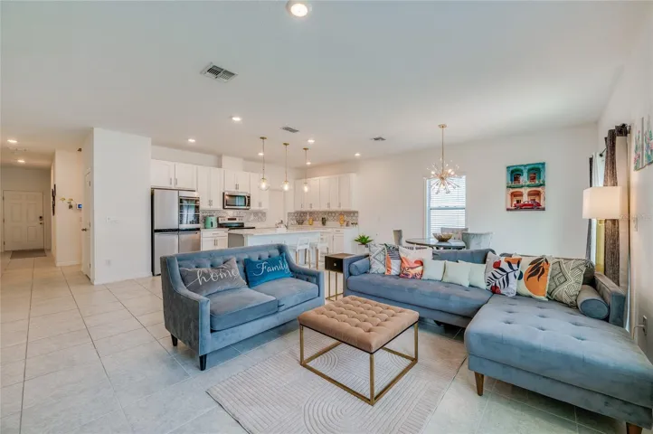Generous open floor plan showing the continuous tiled flooring connecting the main living space directly to the kitchen area. A wide window and a sliding glass door offer views and access to the outdoors.