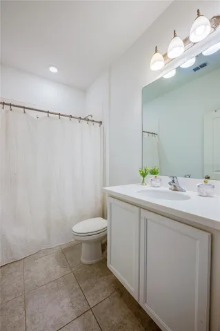 Clean and functional bathroom featuring a white vanity with a solid countertop, a large wall-mounted mirror, and tile flooring. The space includes a standard toilet and a shower-tub combination.