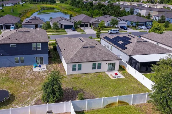Rear aerial view displaying the property's sizable backyard, which features a concrete patio  ideal for outdoor entertaining. The yard is partially enclosed by a white vinyl privacy fence.