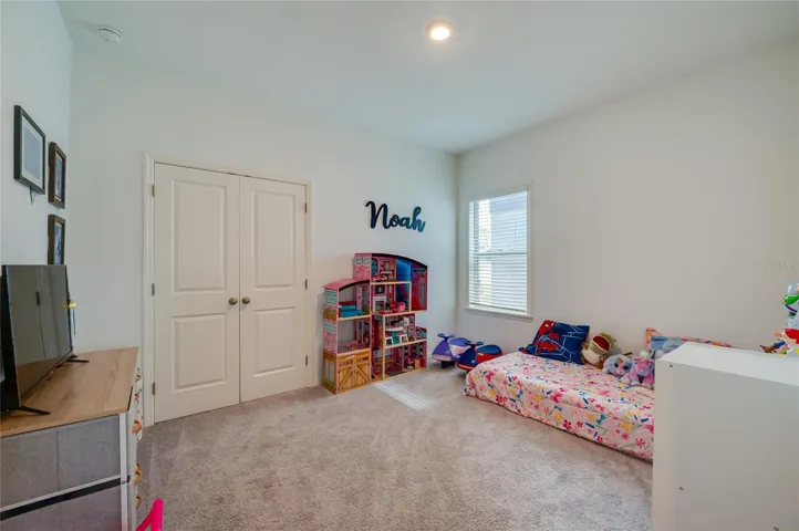 A cheerful bedroom featuring plush carpeting, a large window letting in natural light, and a double-door closet for ample storage.