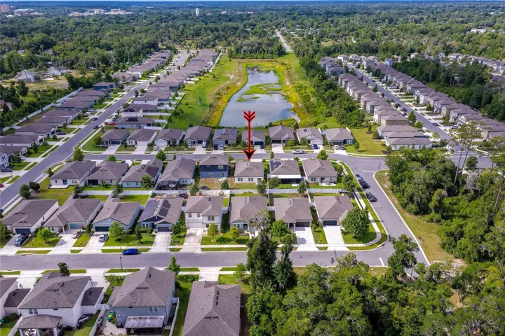 Birds-eye view tracking across the residential development, featuring an expansive retention pond that stretches between the rows of contemporary homes.