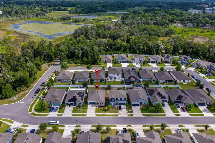 High-angle aerial view showcasing a single-family home within a manicured suburban neighborhood, bordered by a dense green preserve and a scenic natural wetland.