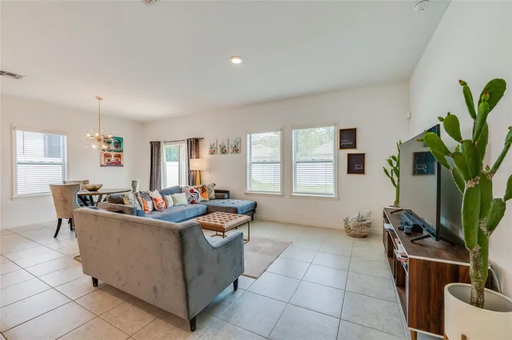 Spacious living area with large windows that provide abundant natural light and look out toward the backyard. The room features neutral tiled flooring and recessed lighting
