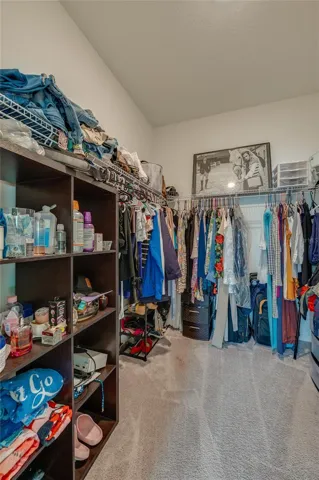 Substantial walk-in master closet complete with built-in wire shelving and hanging racks that offer abundant storage space. The room is fully carpeted and features high ceilings.