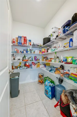 A deep, walk-in pantry equipped with multiple tiers of wire shelving wrapped around the walls for maximum storage efficiency. The space features tiled flooring and bright overhead lighting.