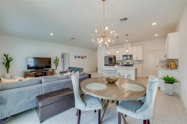 An expansive look from the dining alcove back through the great room toward the kitchen, demonstrating a cohesive design tied together by matching light fixtures and uniform tile flooring.