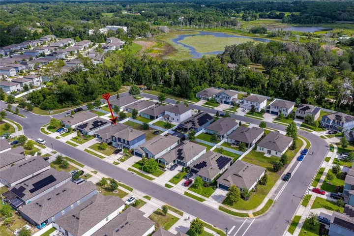 Elevated perspective capturing the layout of modern residential streets and neatly aligned homes, positioned perfectly near a large, tranquil pond.