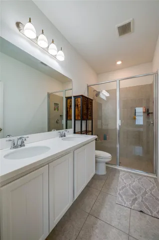 Modern master bathroom boasting a wide double vanity with crisp white cabinetry and a large  mirror. The space is anchored by a spacious walk-in shower lined with neutral tile.