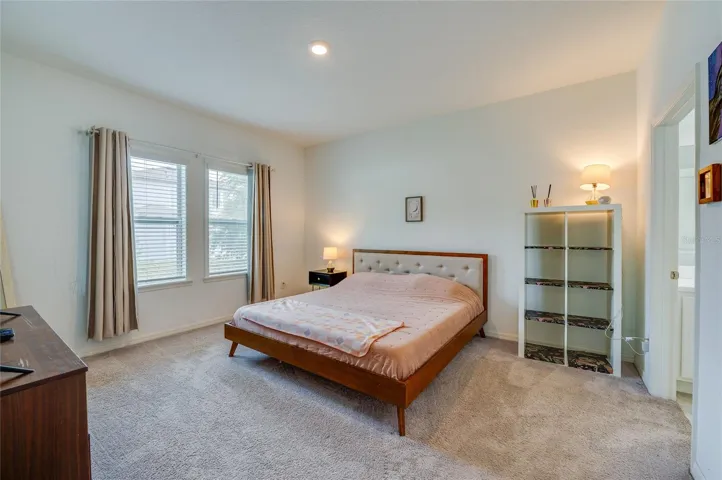 Bright and spacious primary bedroom featuring plush carpeting, soft neutral walls, and windows that invite ample natural light. An attached en-suite bathroom provides seamless convenience.