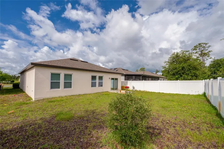 Spacious back exterior view of the home showing a wide, grassy lawn and a  tall white privacy fence. The rear of the house features neutral walls, multiple windows, and a sliding glass door that opens to the yard.