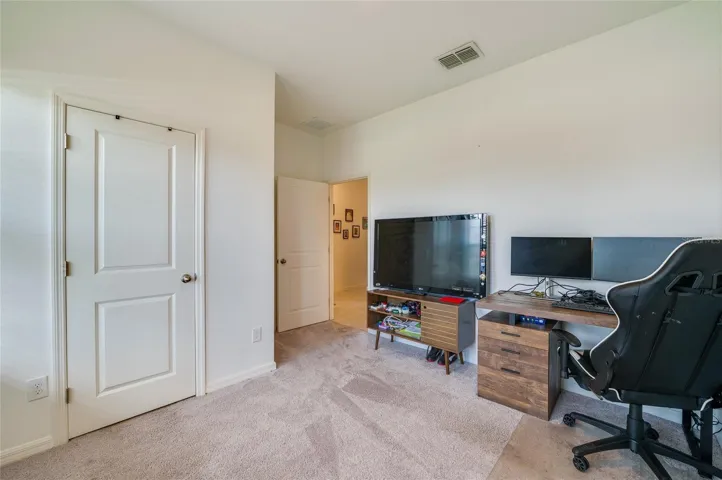 A versatile bedroom showcasing neutral carpet flooring, recessed lighting, and a view into the main hallway through an open doorway. A separate closet door provides convenient storage within the room.