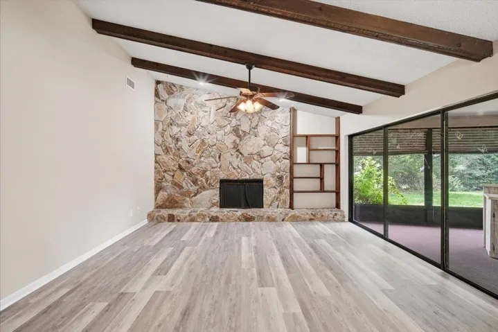 Impressive family room with soaring ceilings with stone fireplace, beams and triple sliding glass doors