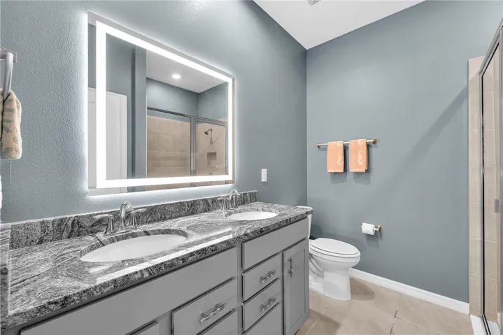This luxurious en-suite bathroom features dual sinks, spacious vanity with granite and a touch-activated and LED lighted mirror, a large shower with built-in bench and linen closet for additional storage.