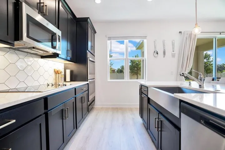 The GOURMET KITCHEN is a true showstopper, featuring BUILT-IN DOUBLE OVENS, a cooktop, stone countertops, a stylish tile backsplash, stainless steel appliances, a closet pantry, and a large island with a FARMHOUSE SINK and breakfast bar seating.