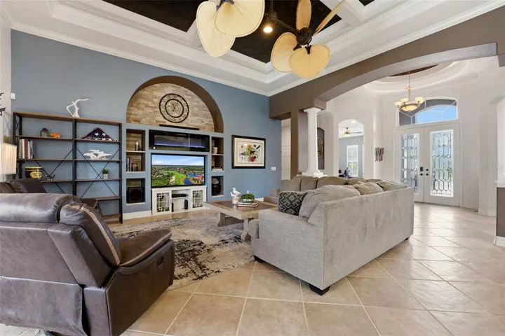 Large great room with fireplace, built-ins, double tray ceiling, crown molding, custom ceiling detail and double paddle fan.