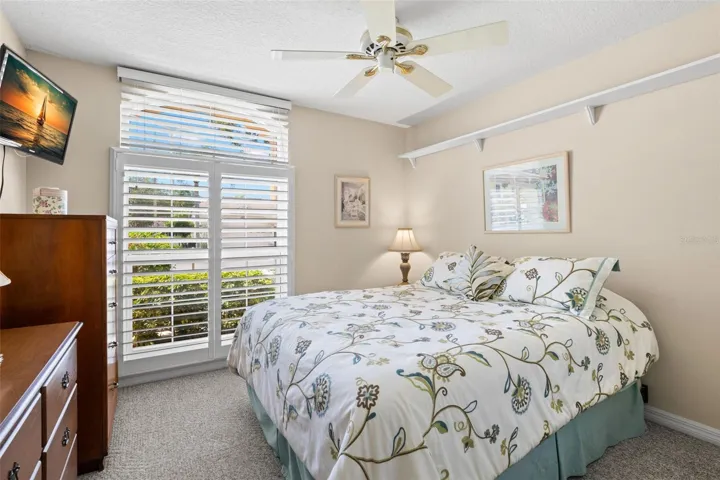 Natural light filters through plantation shutters in this well-proportioned third bedroom with ceiling fan and closet storage.