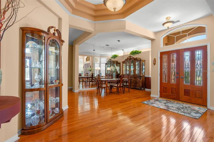 The inviting foyer features hardwood flooring, a dramatic tray ceiling, and a beautiful wood double-door entry framed by transom windows.