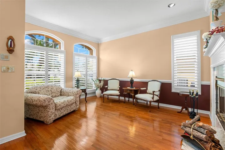 Plantation shutters, arched transom windows, crown molding, and hardwood flooring enhance the living room's timeless appeal.