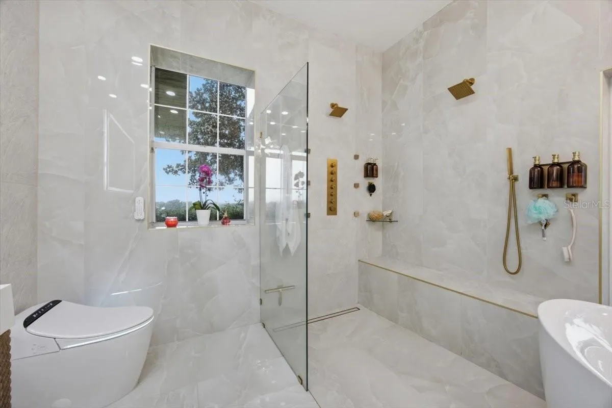 Resort-inspired spa shower featuring an oversized walk-in design with dual rainfall shower heads, multiple body spray jets, a handheld wand, an expansive built-in tiled bench, frameless glass enclosure, and floor-to-ceiling porcelain tile for a truly luxurious experience.