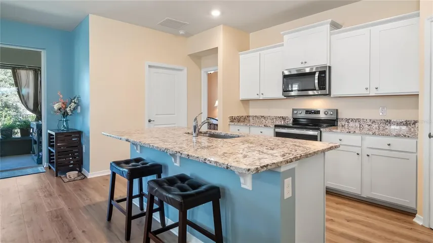 The kitchen is equipped with stainless steel appliances, granite countertops, and a breakfast bar overlooking the living room and dining room.