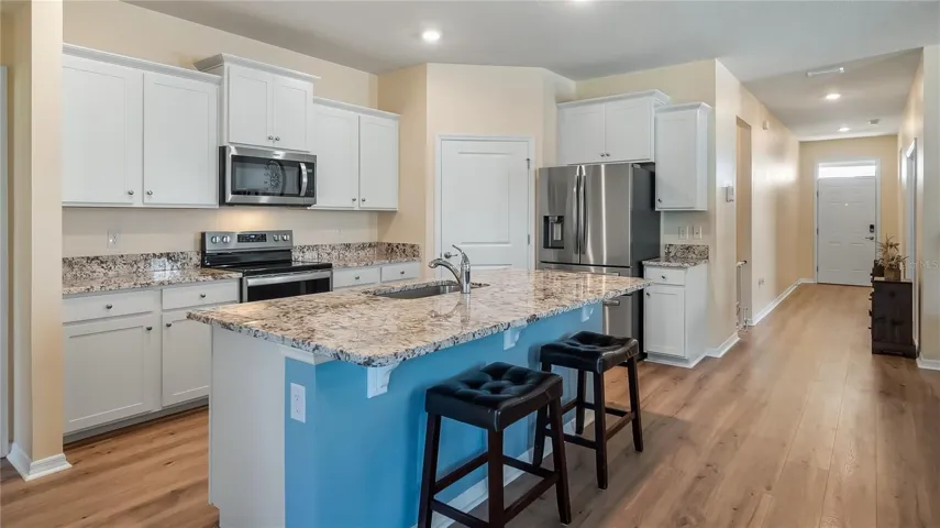 The kitchen is equipped with stainless steel appliances, granite countertops, and a breakfast bar overlooking the living room and dining room.