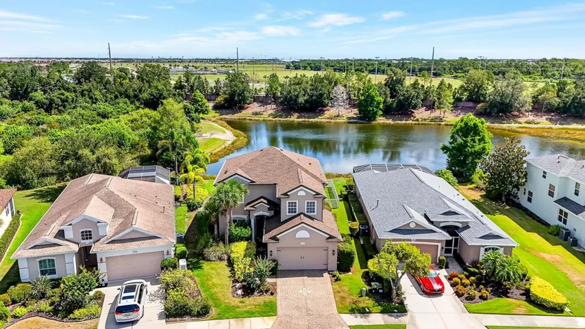 Aerial view facing front of home showing lake and mature landscaping all around it.