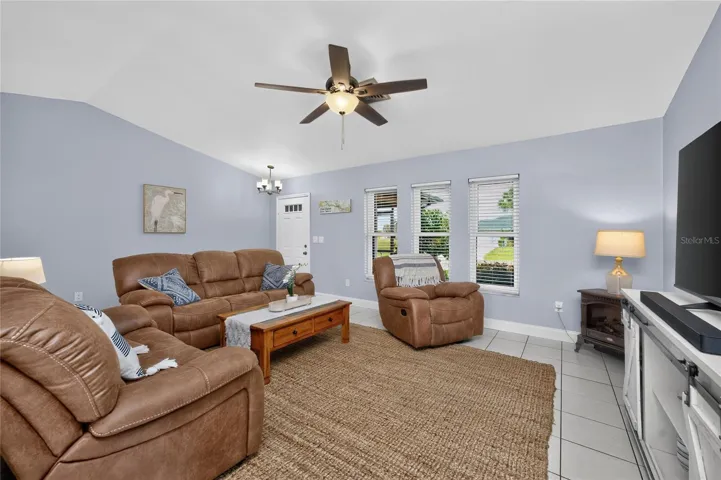 The living room has a cathedral ceiling, ceiling fan and tiled flooring.