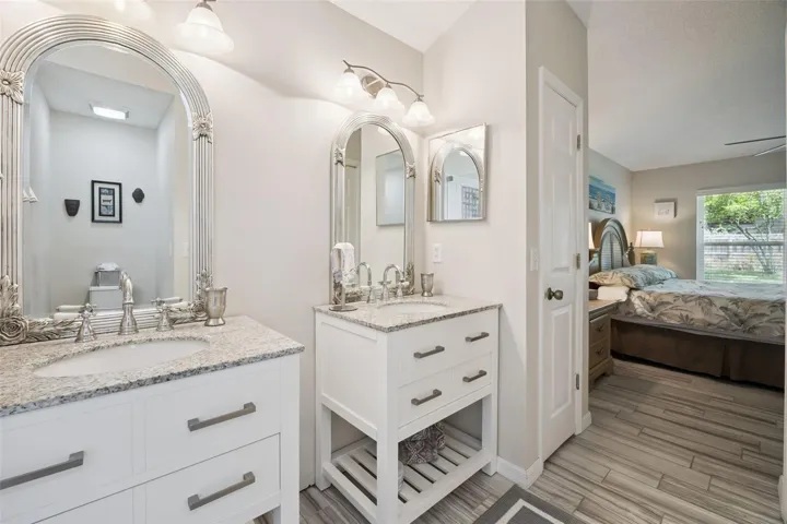 Updated primary bathroom with dual vanities, granite countertops, stylish mirrors, updated fixtures, and bright lighting.